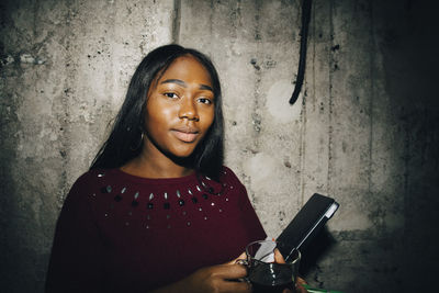 Portrait of female entrepreneur with laptop standing against wall at workplace