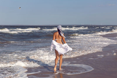 Woman run in a white swimsuit and hat sunglasses on an empty sandy beach