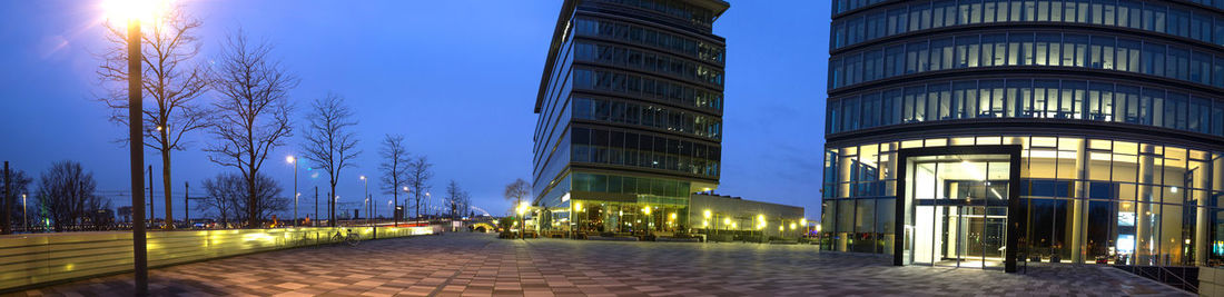 Illuminated street amidst buildings against sky at dusk