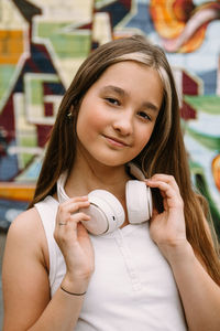 Teen girl with headphones posing on colorful city graffiti background, looking at camera