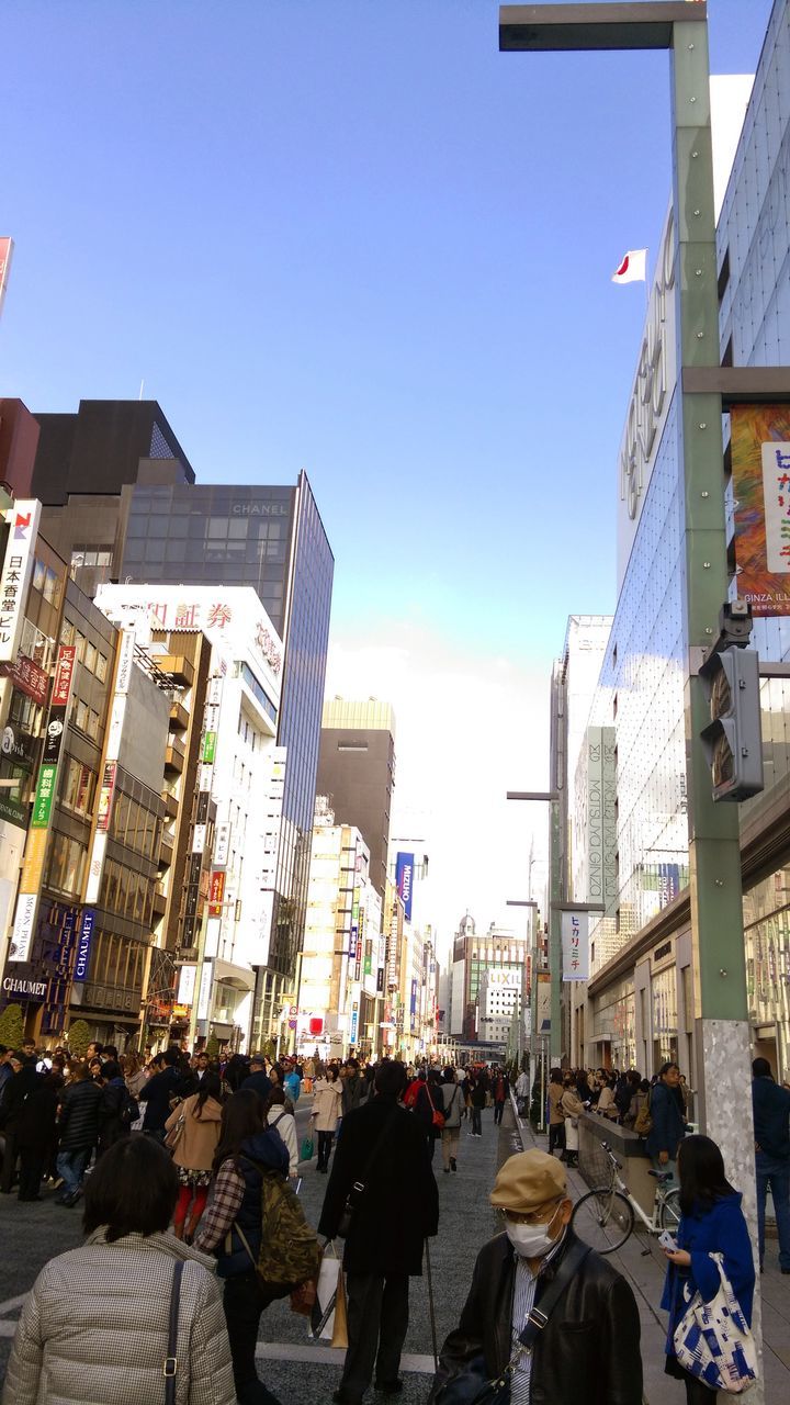 building exterior, architecture, built structure, city, clear sky, large group of people, men, street, city life, person, residential building, residential structure, building, sunlight, walking, sky, lifestyles, day, residential district