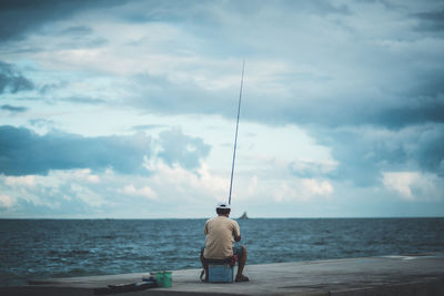 Rear view of man fishing in sea against sky