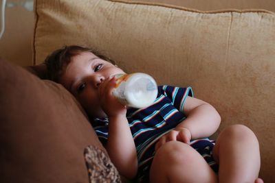 Boy drinking milk while sitting on sofa at home