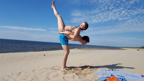 Man carrying woman while standing on sand at beach