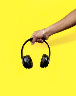 Cropped hand of woman holding headphones against yellow background