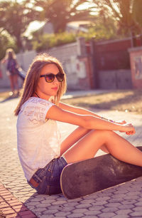 Portrait of young girl with short shorts and skateboard sitting outdoors on a hot summer day