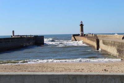 Lighthouse by sea against clear sky