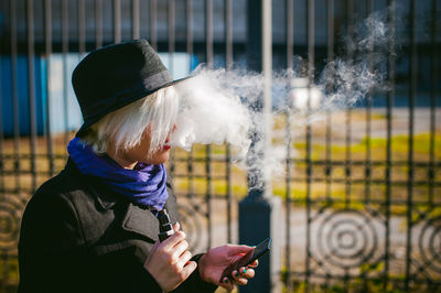 Young woman using mobile phone while smoking at park