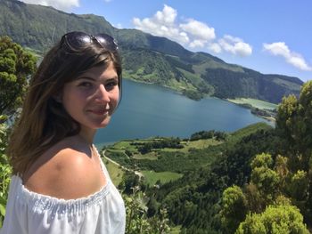 Portrait of young woman standing against mountains and lake