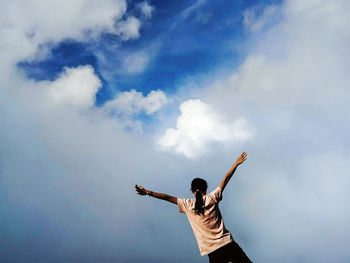 Rear view of man with arms outstretched standing against sky