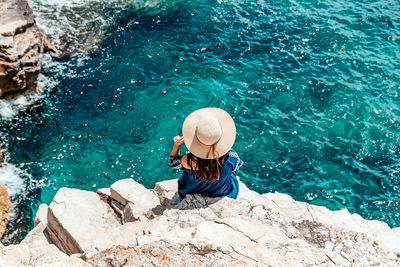 High angle view of woman sitting on rock by sea