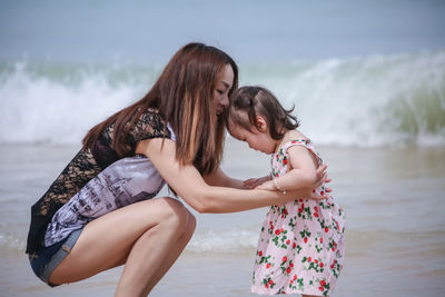 Young woman with daughter standing in sea against sky