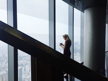 Woman photographing through smart phone while standing by window