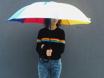 Woman holding umbrella while standing against concrete wall