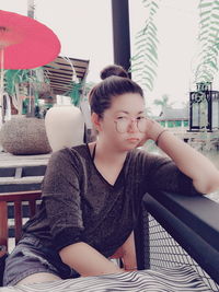 Portrait of young woman leaning on railing while sitting at sidewalk cafe