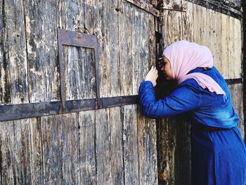 Woman peeking through closed wooden gate