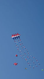 Low angle view of kites flying against clear blue sky