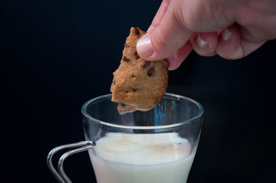 Close-up of hand holding chocolate cookie with black background