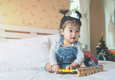 Portrait of cute girl sitting on bed at home