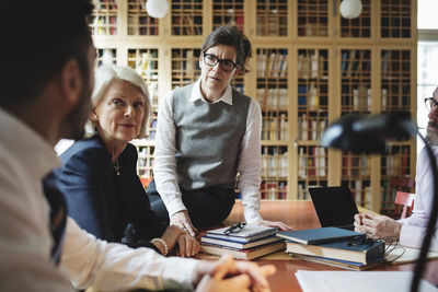 Female lawyers listening to coworker sitting at table in library