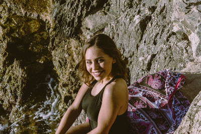 Portrait of smiling young woman sitting by rock formation