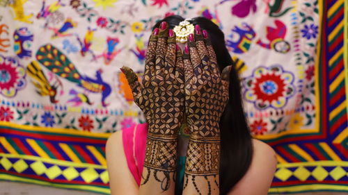 Close-up of bride with henna tattoo hiding face with hands