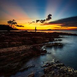 Silhouette people standing on rock by sea against sky during sunset