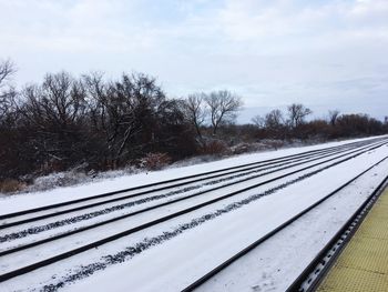 Railway tracks by snow covered landscape against sky