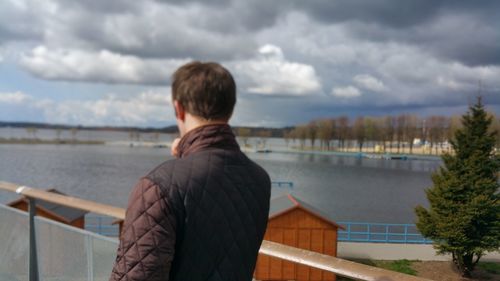 Rear view of man standing on pier by lake against cloudy sky