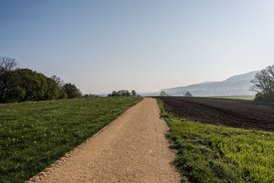 Empty road amidst field against clear sky