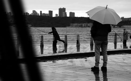 Rear view of silhouette man fishing against sky in city