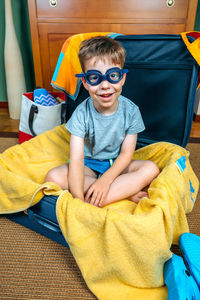 Boy wearing eyewear sitting in open suitcase