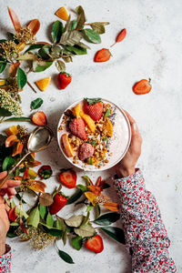 From above of unrecognizable female with smoothie bowl with fruits and berries sitting at table during breakfast in morning