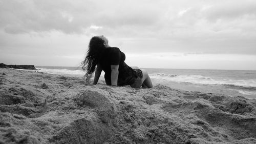 Woman relaxing on shore at beach against sky