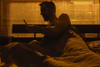 Side view of man sitting on bed at home