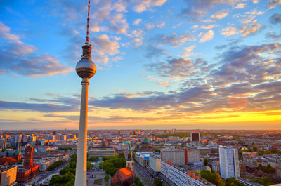 Communications tower in city against sky during sunset