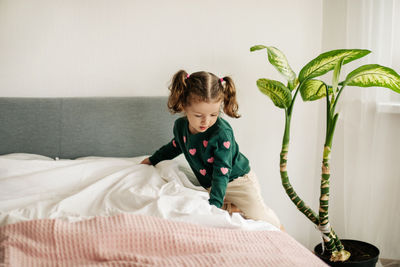 A little girl with two ponytails makes her bed in the morning after waking up