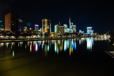 Illuminated buildings by river against sky at night