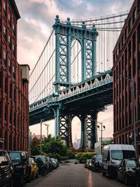 Low angle view of manhattan bridge in city against cloudy sky
