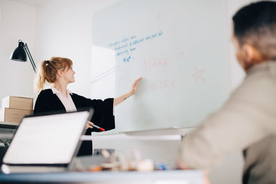 Low angle view of young businesswoman standing by acrylic glass with colleague in board room at office