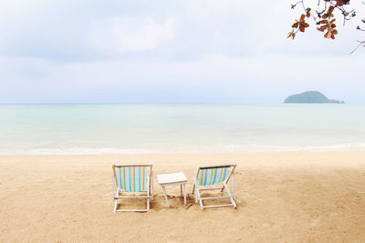 Deck chairs on beach against sky