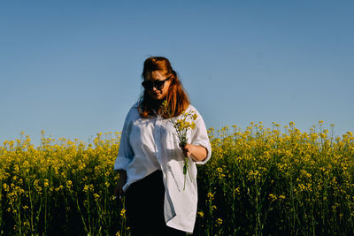 Portrait of young woman standing on field against clear sky