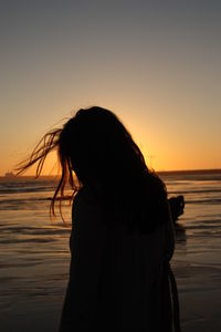 Woman at beach against sky during sunset