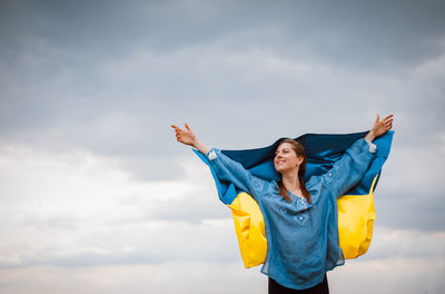 Smiling woman holding ukrainian flag against sky