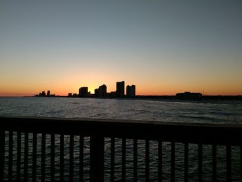 Silhouette of city at waterfront during sunset