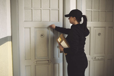 Side view of delivery woman with package knocking at door