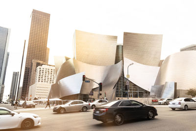 Cars on road by buildings against sky in city