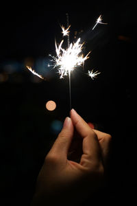 Close-up of hand holding sparkler against sky at night