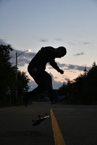 Silhouette man skateboarding on road against sky during sunset