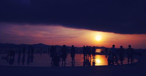 Silhouette people on beach against sky during sunset